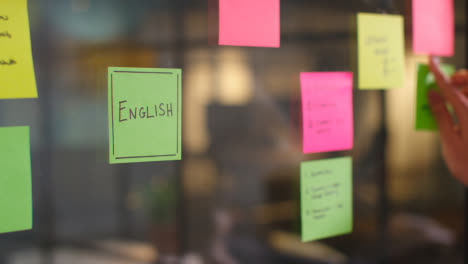 Close-Up-Of-Woman-Putting-Sticky-Note-With-English-Written-On-It-Onto-Transparent-Screen-In-Office-2