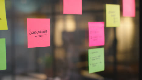 Close-Up-Of-Woman-Putting-Sticky-Note-With-Scholarship-Written-On-It-Onto-Transparent-Screen-In-Office-2