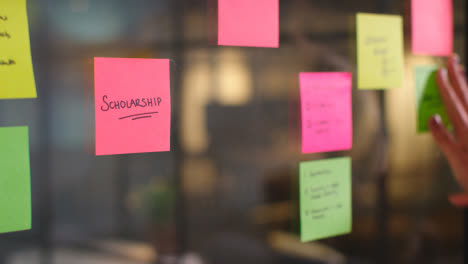 Close-Up-Of-Woman-Putting-Sticky-Note-With-Scholarship-Written-On-It-Onto-Transparent-Screen-In-Office-3