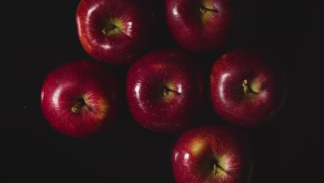 Obenliegende-Studioaufnahme-Einer-Hand,-Die-Den-Roten-Apfel-Ersetzt,-Der-Sich-Vor-Schwarzem-Hintergrund-Dreht