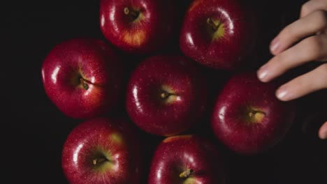 Overhead-Studio-Shot-Of-Hand-Picking-From-Circle-Of-Red-Apples-Against-Black-Background