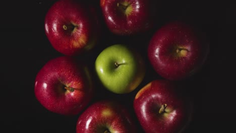 Overhead-Studio-Shot-Of-Hand-Picking-From-Red-And-Green-Apples-Revolving-Against-Black-Background