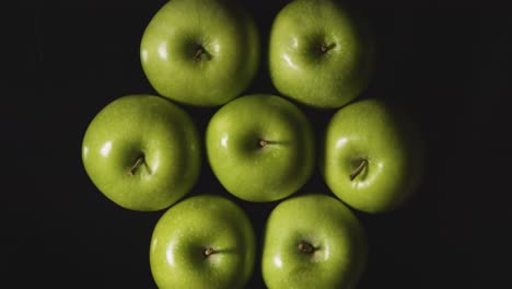 Overhead-Studio-Shot-Of-Hand-Picking-From-Green-Apples-Revolving-Against-Black-Background