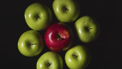 Obenliegende-Studioaufnahme-Von-Rotem-Apfel-Im-Kreis-Von-Grünen-Äpfeln,-Die-Sich-Vor-Schwarzem-Hintergrund-Drehen