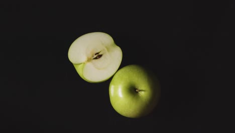 Overhead-Studio-Shot-Of-Whole-And-Halved-Green-Apple-Revolving-Against-Black-Background