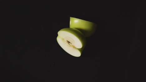 Obenliegende-Studioaufnahme-Eines-Halbierten-Grünen-Apfels,-Der-Sich-Vor-Schwarzem-Hintergrund-Dreht