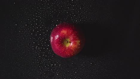 Obenliegende-Studioaufnahme-Von-Rotem-Apfel-Mit-Wassertröpfchen,-Die-Sich-Vor-Schwarzem-Hintergrund-Drehen