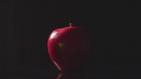 Studioaufnahme-Einer-Hand,-Die-Einen-Roten-Apfel-Aufhebt,-Der-Sich-Vor-Schwarzem-Hintergrund-Dreht