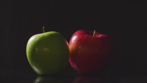 Studioaufnahme-Einer-Hand,-Die-Zwischen-Roten-Und-Grünen-Äpfeln-Wählt,-Die-Sich-Vor-Schwarzem-Hintergrund-Drehen