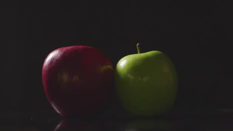 Studioaufnahme-Einer-Hand,-Die-Einen-Grünen-Apfel-Neben-Einen-Roten-Apfel-Legt,-Der-Sich-Vor-Schwarzem-Hintergrund-Dreht