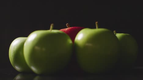 Foto-De-Estudio-De-Manzana-Roja-En-Círculo-De-Manzanas-Verdes-Girando-Contra-Fondo-Negro