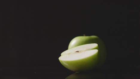 Foto-De-Estudio-De-Manzana-Verde-Entera-Y-Cortada-A-La-Mitad-Girando-Contra-Fondo-Negro