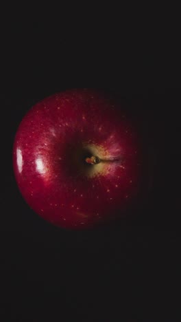 Vertical-Video-Overhead-Studio-Shot-Of-Red-Apple-Revolving-Against-Black-Background