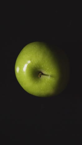 Vertical-Video-Overhead-Studio-Shot-Of-Green-Apple-Revolving-Against-Black-Background