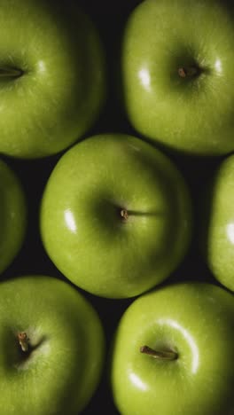 Vertical-Video-Overhead-Studio-Shot-Of-Green-Apples-Revolving-Against-Black-Background