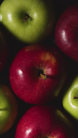 Vertical-Video-Overhead-Studio-Shot-Of-Green-And-Red-Apples-Revolving-Against-Black-Background-1