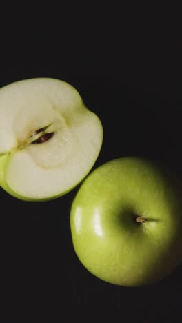 Toma-De-Estudio-De-Video-Vertical-De-Una-Manzana-Verde-Entera-Y-Partida-En-Dos-Girando-Contra-Un-Fondo-Negro