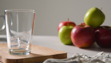 Jugo-De-Manzana-Que-Se-Vierte-En-Un-Vaso-Con-Hielo-Y-Manzanas-Frescas-En-El-Fondo