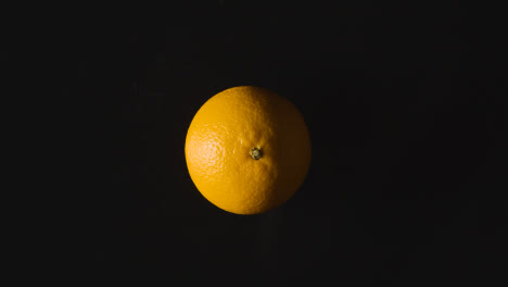 Obenliegende-Studioaufnahme-Von-Orange,-Die-Sich-Vor-Schwarzem-Hintergrund-Dreht