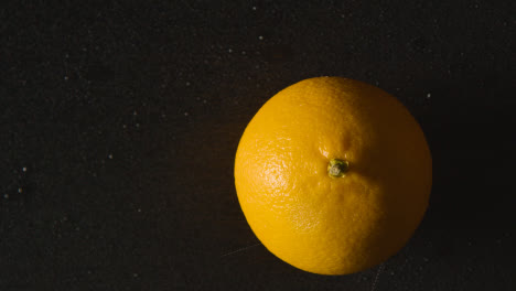 Overhead-Studio-Shot-Of-Orange-Being-Sprayed-With-Water-Revolving-Against-Black-Background