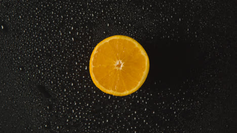 Obenliegende-Studioaufnahme-Einer-Orangefarbenen-Hälfte-Mit-Wassertröpfchen,-Die-Sich-Vor-Schwarzem-Hintergrund-Drehen