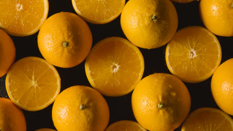 Overhead-Studio-Shot-Of-Whole-And-Halved-Oranges-With-Water-Droplets-Against-Black-Background