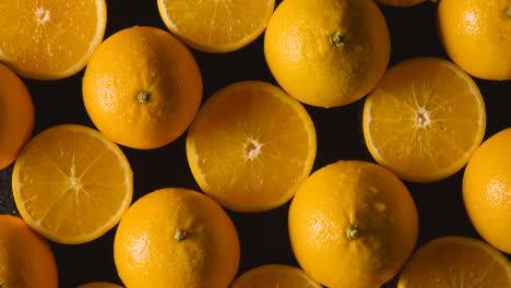 Overhead-Studioaufnahme-Von-Ganzen-Und-Halbierten-Orangen-Mit-Wassertropfen-Vor-Schwarzem-Hintergrund