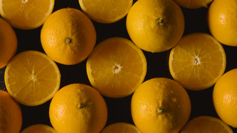 Overhead-Studio-Shot-Of-Hand-With-Whole-And-Halved-Oranges-With-Water-Droplets-Against-Black-Background