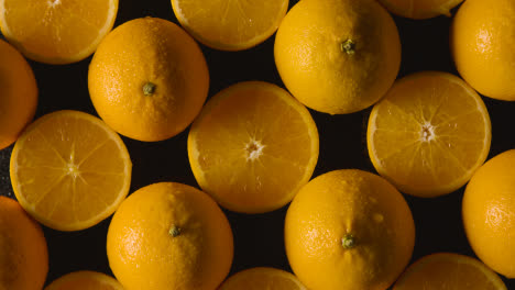 Foto-De-Estudio-Superior-De-La-Mano-Con-Naranjas-Enteras-Y-Partidas-A-La-Mitad-Con-Gotas-De-Agua-Sobre-Fondo-Negro