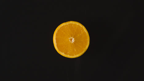 Obenliegende-Studioaufnahme-Einer-Orangefarbenen-Hälfte,-Die-Sich-Vor-Schwarzem-Hintergrund-Dreht