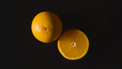 Overhead-Studioaufnahme-Von-Ganzen-Und-Halbierten-Orangen-Vor-Schwarzem-Hintergrund