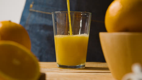 Nahaufnahme-Eines-Mannes,-Der-Frischen-Orangensaft-In-Ein-Glas-Mit-Eis-Mit-Orangen-Im-Vordergrund-Gießt