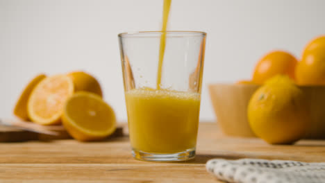 Nahaufnahme-Eines-Mannes,-Der-Frischen-Orangensaft-In-Ein-Glas-Mit-Eis-Gießt,-Mit-Orangen-Im-Vordergrund-2