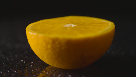 Studio-Shot-Of-Orange-Half-With-Water-Droplets-Revolving-Against-Black-Background