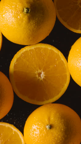 Vertical-Video-Overhead-Studio-Shot-Of-Whole-And-Halved-Oranges-Against-Black-Background