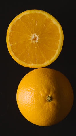 Vertical-Video-Overhead-Studio-Shot-Of-Whole-And-Halved-Oranges-Against-Black-Background-1