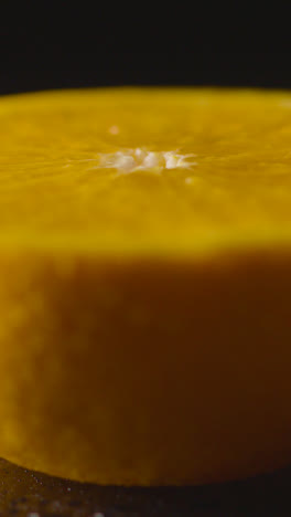 Vertical-Video-Close-Up-Shot-Of-Orange-Half-With-Water-Droplets-Revolving-Against-Black-Background