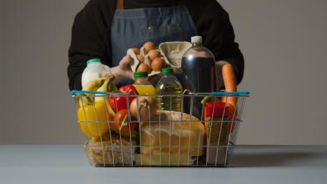Studio-Shot-Of-Shop-Worker-Checking-Basic-Food-Items-In-Supermarket-Wire-Shopping-Basket-
