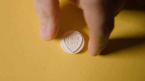 Hand-Picking-Up-Heart-Candy-With-True-Love-Message-On-Yellow-Background