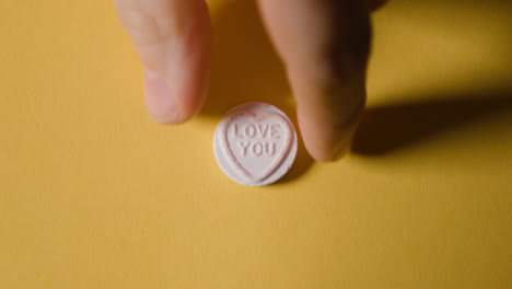 Hand-Picking-Up-Heart-Candy-With-Love-You-Message-On-Yellow-Background