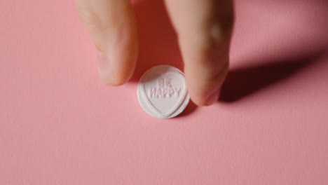 Hand-Picking-Up-Heart-Candy-With-Be-Happy-Message-On-Pink-Background