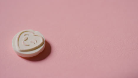 Recogiendo-A-Mano-Caramelos-De-Corazón-Con-Emoji-Guiño-Romántico-Sobre-Fondo-Rosa