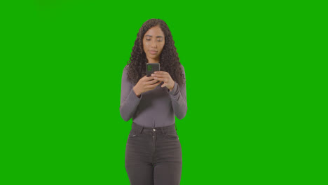 Three-Quarter-Length-Portrait-Of-Woman-Text-Messaging-On-Mobile-Phone-Against-Green-Screen