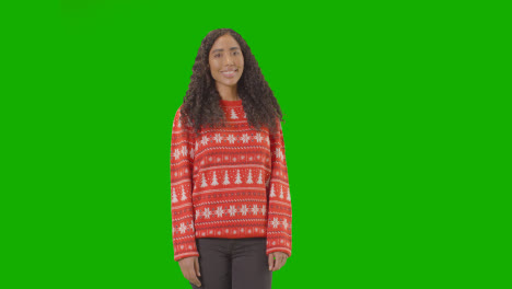 Studioporträt-Einer-Frau-Mit-Weihnachtspullover-Vor-Grünem-Bildschirm,-Die-In-Die-Kamera-Lächelt-Und-Frohe-Weihnachten-Sagt