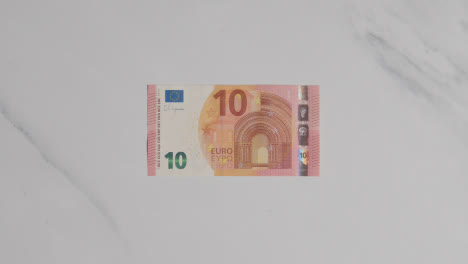 Overhead-Währungsaufnahme-Einer-Hand,-Die-Einen-10-Euro-Schein-Auf-Einer-Marmoroberfläche-Ergreift
