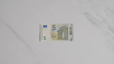 Overhead-Währungsaufnahme-Einer-Hand,-Die-Einen-5-Euro-Schein-Auf-Einer-Marmoroberfläche-Ergreift