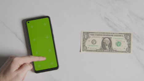 Overhead-Currency-Shot-Of-US-1-Dollar-Bill-Next-To-Person-Using-Green-Screen-Mobile-Phone
