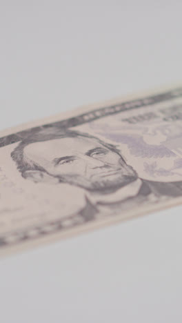 Vertical-Video-Close-Up-Currency-Shot-Of-Hand-Grabbing-US-5-Dollar-Bill-On-Marble-Background