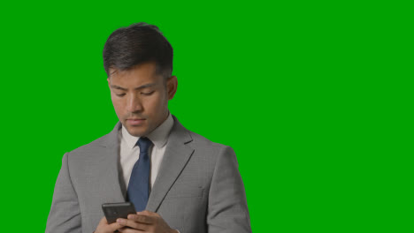 Portrait-Of-Businessman-In-Suit-Against-Green-Screen-Messaging-On-Mobile-Phone-1