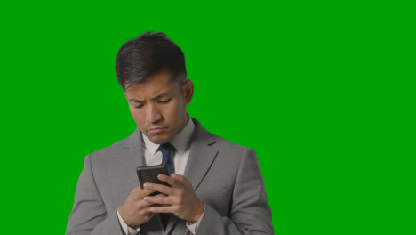 Portrait-Of-Serious-Businessman-In-Suit-Against-Green-Screen-Messaging-On-Mobile-Phone-